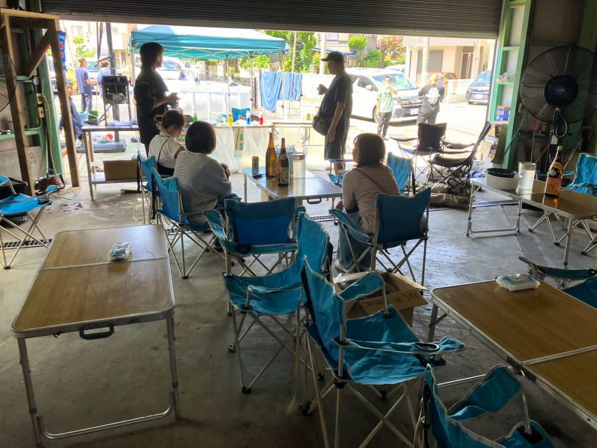 会社の敷地でテーブルを囲ぬバーベキューを楽しんでいる様子
